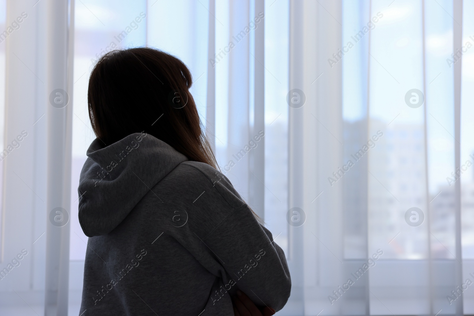 Photo of Loneliness concept. Sad woman near window at home, back view. Space for text