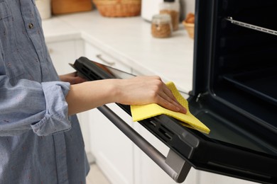 Photo of Woman cleaning oven door with rag in kitchen, closeup