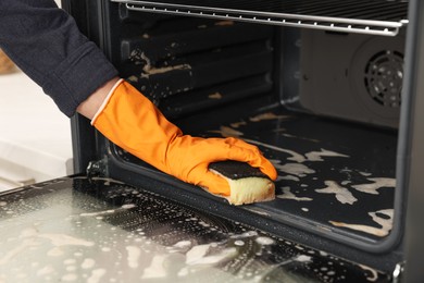 Photo of Woman cleaning oven with sponge in kitchen, closeup