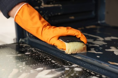 Photo of Woman cleaning oven with sponge in kitchen, closeup