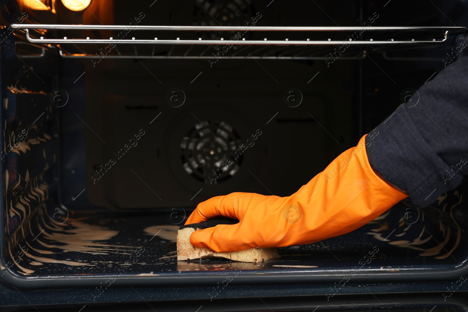 Photo of Woman cleaning oven with sponge, closeup view