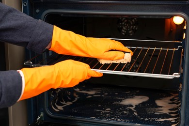 Photo of Woman cleaning oven rack with sponge, closeup