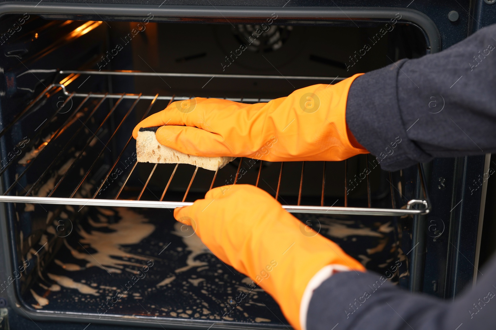 Photo of Woman cleaning oven rack with sponge, closeup