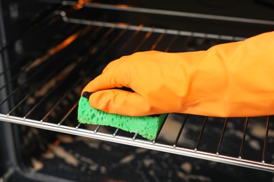 Photo of Woman cleaning oven rack with sponge, closeup