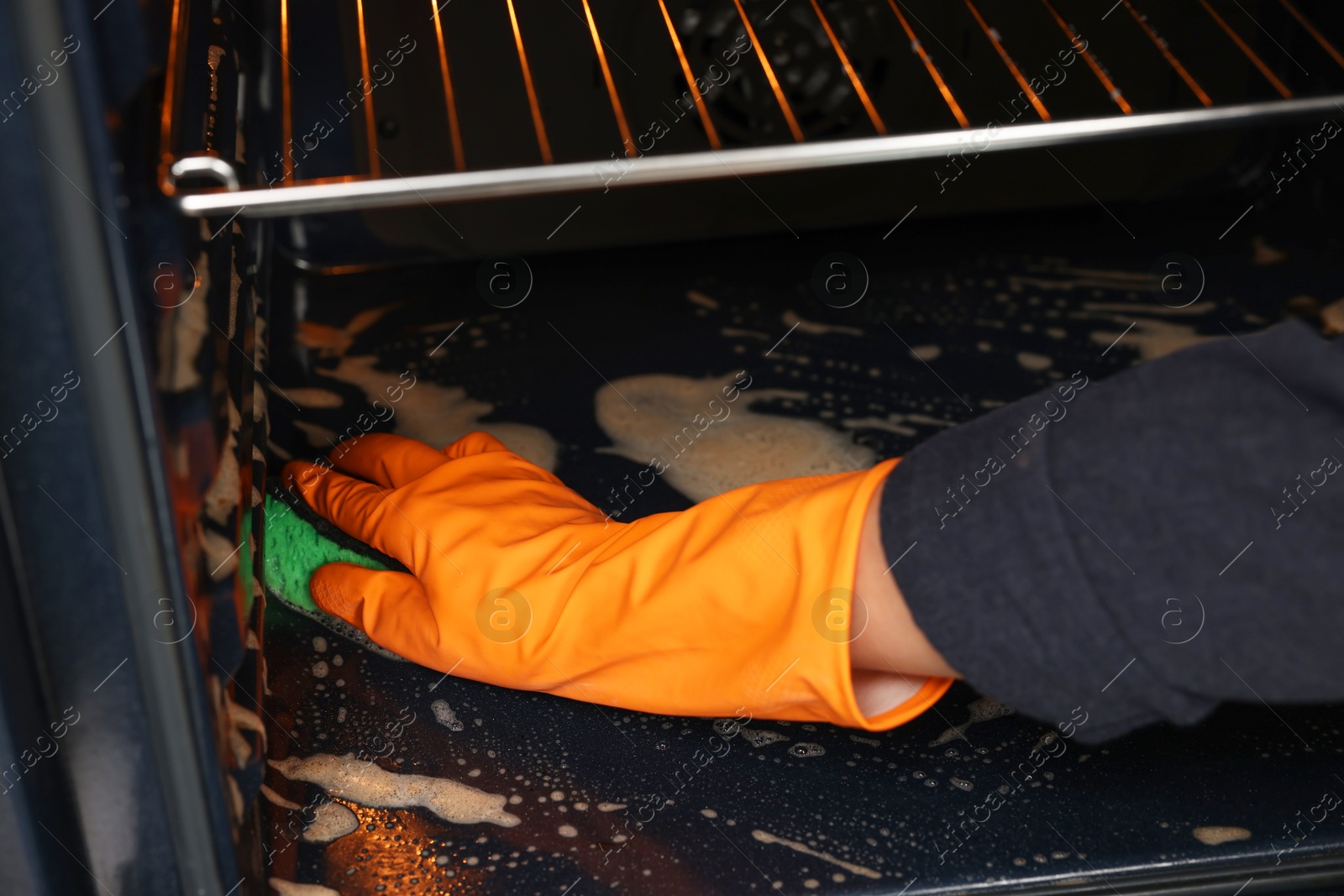 Photo of Woman cleaning oven with sponge, closeup view