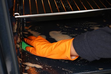 Photo of Woman cleaning oven with sponge, closeup view