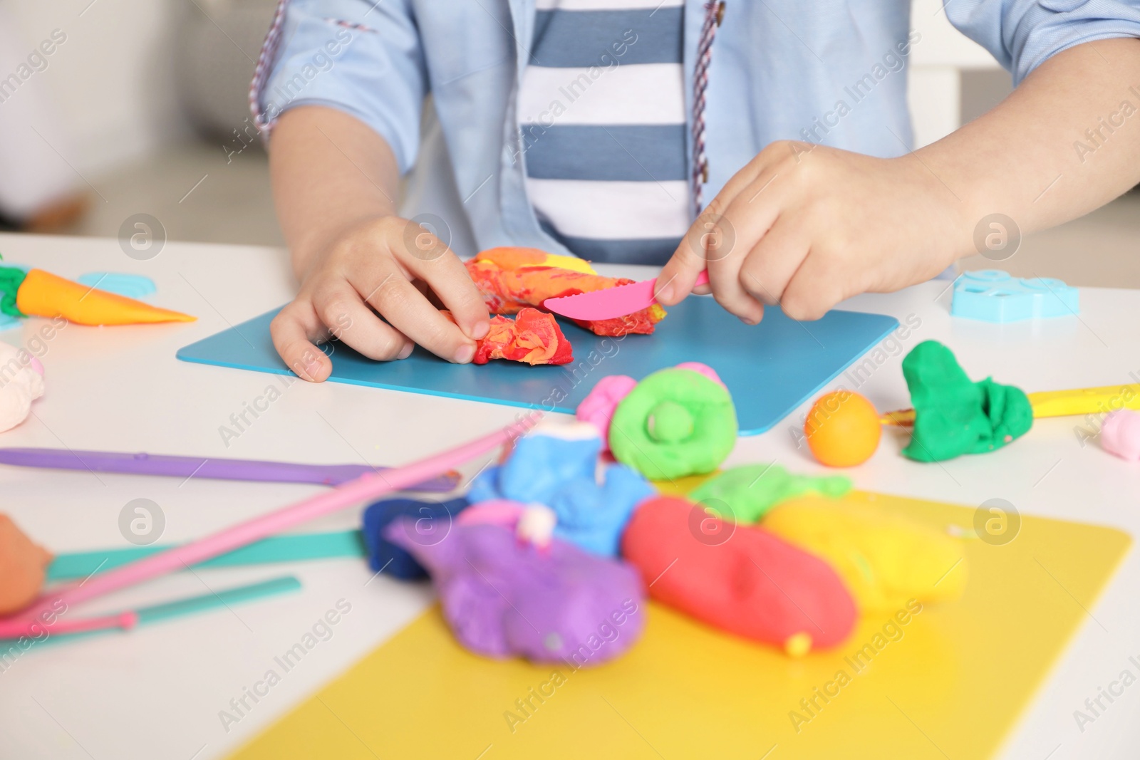 Photo of Little boy sculpting with play dough at table indoors, closeup