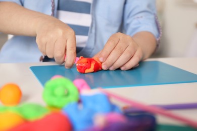 Little boy sculpting with play dough at table indoors, closeup