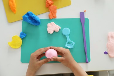 Photo of Little girl sculpting with play dough at white table, top view