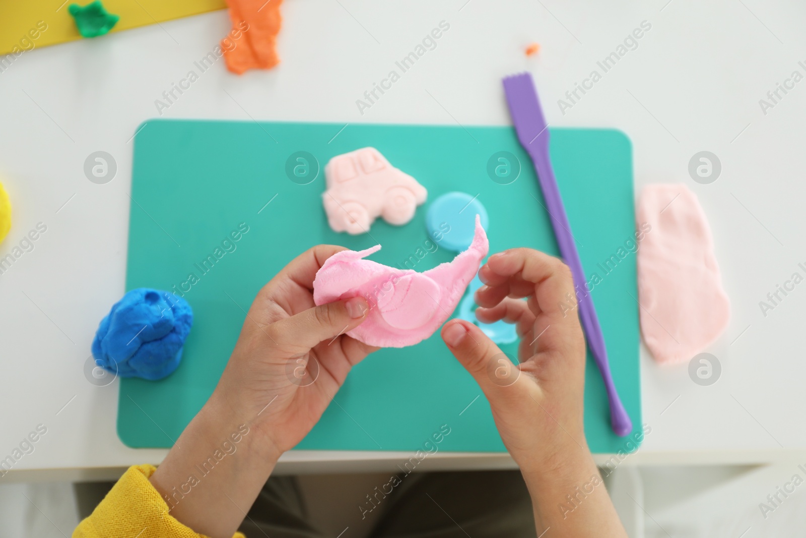 Photo of Little girl sculpting with play dough at white table, top view