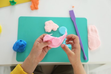 Little girl sculpting with play dough at white table, top view