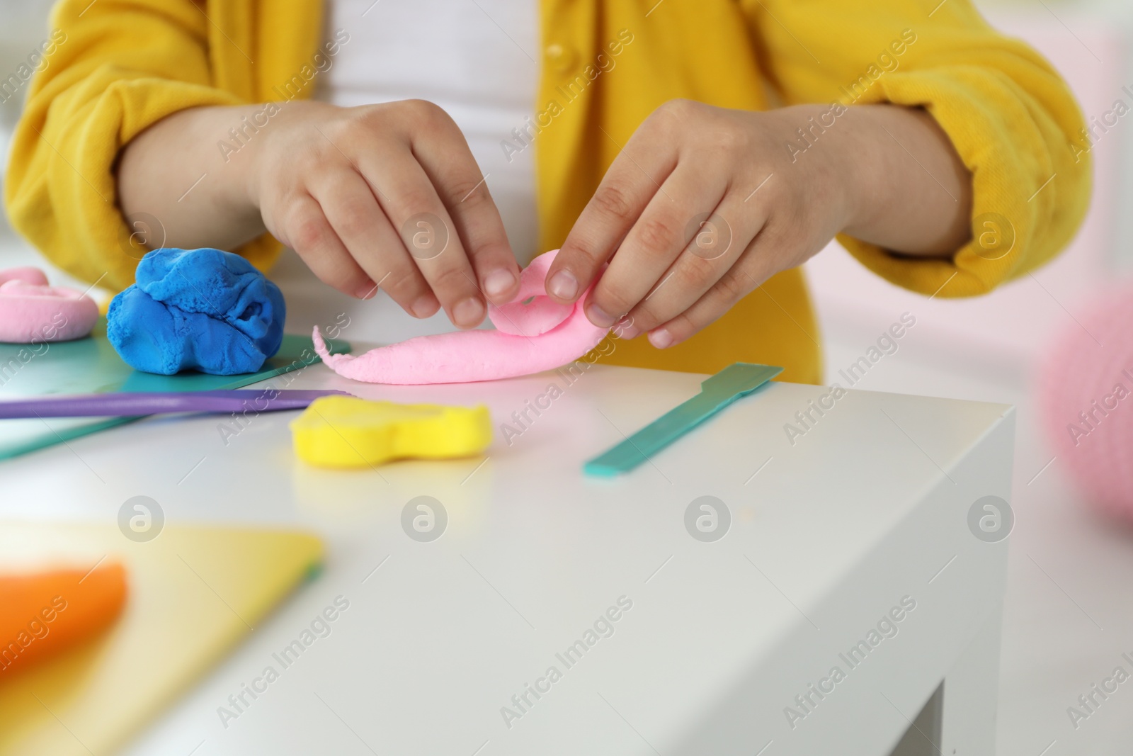 Photo of Little girl sculpting with play dough at white table indoors, closeup