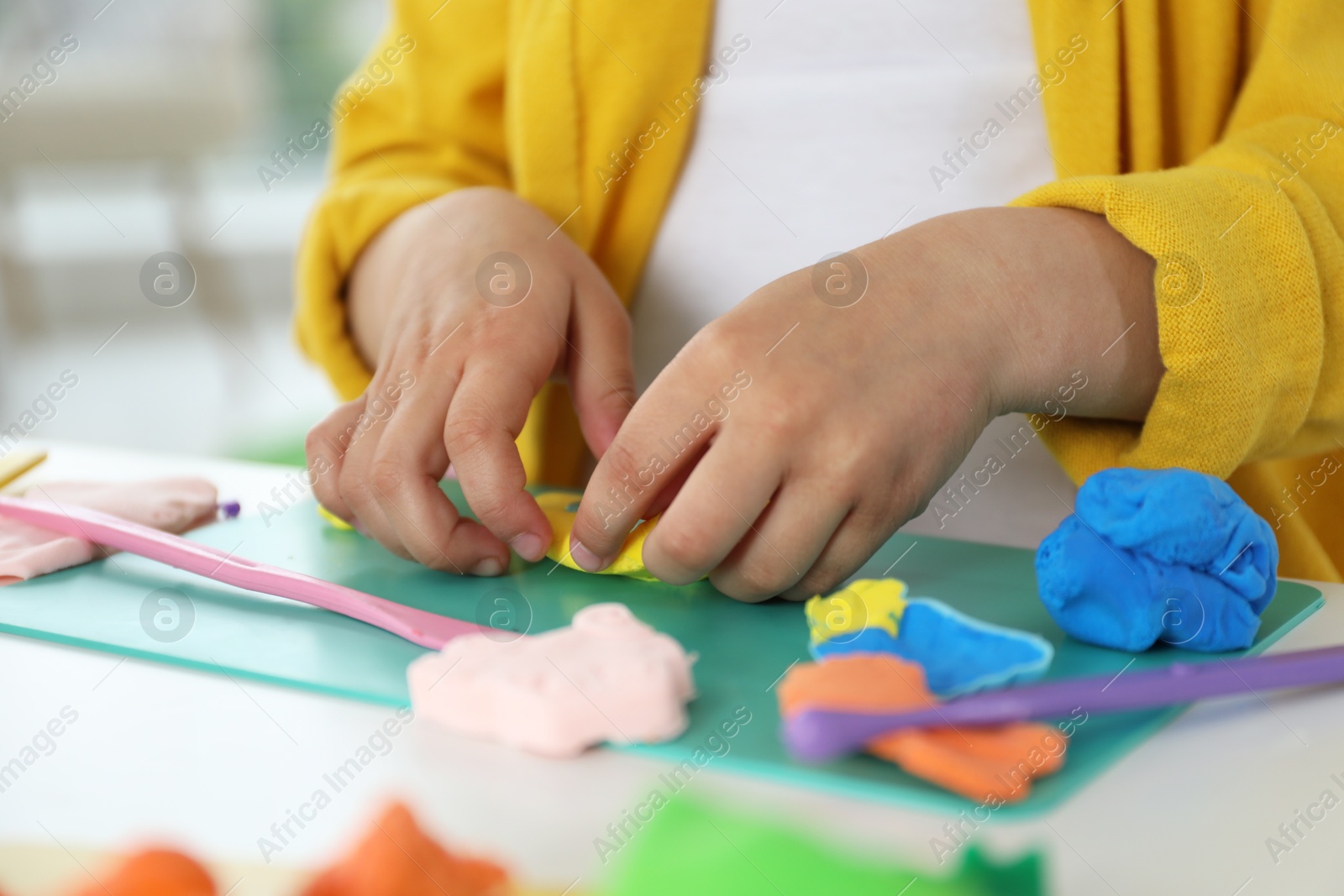 Photo of Little girl sculpting with play dough at table indoors, closeup