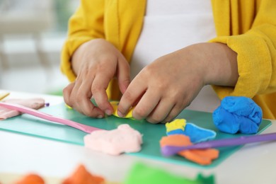 Little girl sculpting with play dough at table indoors, closeup