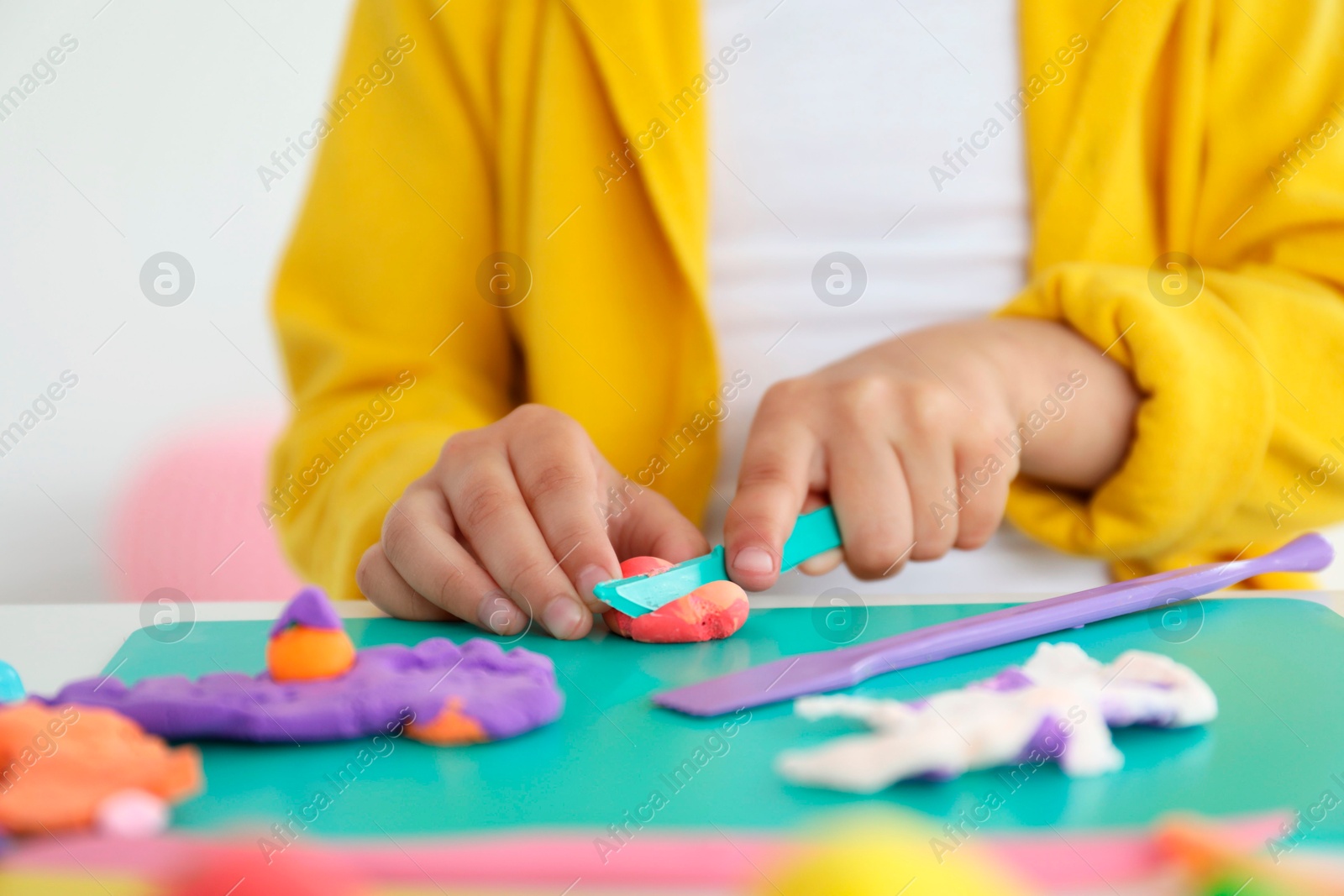 Photo of Little girl sculpting with play dough at table indoors, closeup