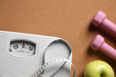 Photo of Scale, measuring tape, dumbbells and fresh apple on brown textured background, flat lay