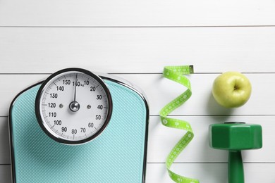 Photo of Scale, measuring tape, dumbbells and fresh apple on white wooden background, flat lay