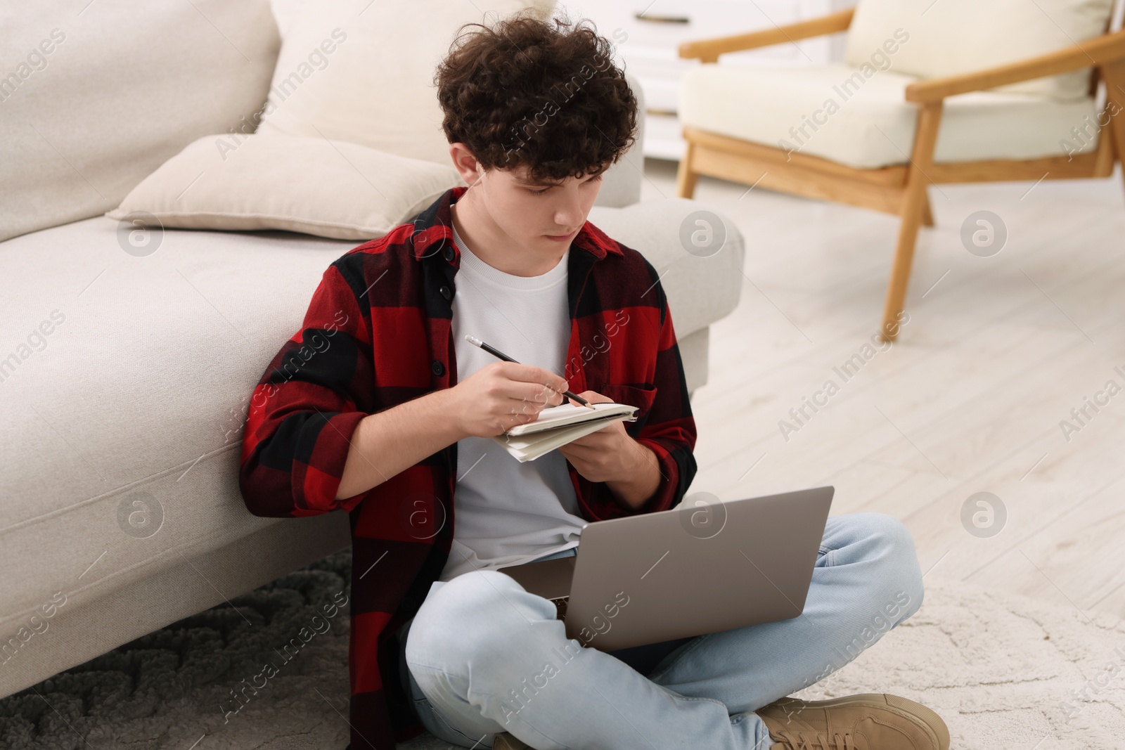 Photo of Teenager taking notes while working with laptop at home. Remote job