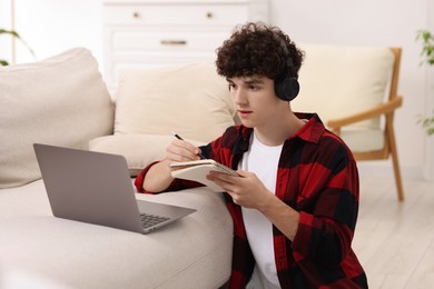 Photo of Teenager in headphones taking notes while working with laptop at home. Remote job