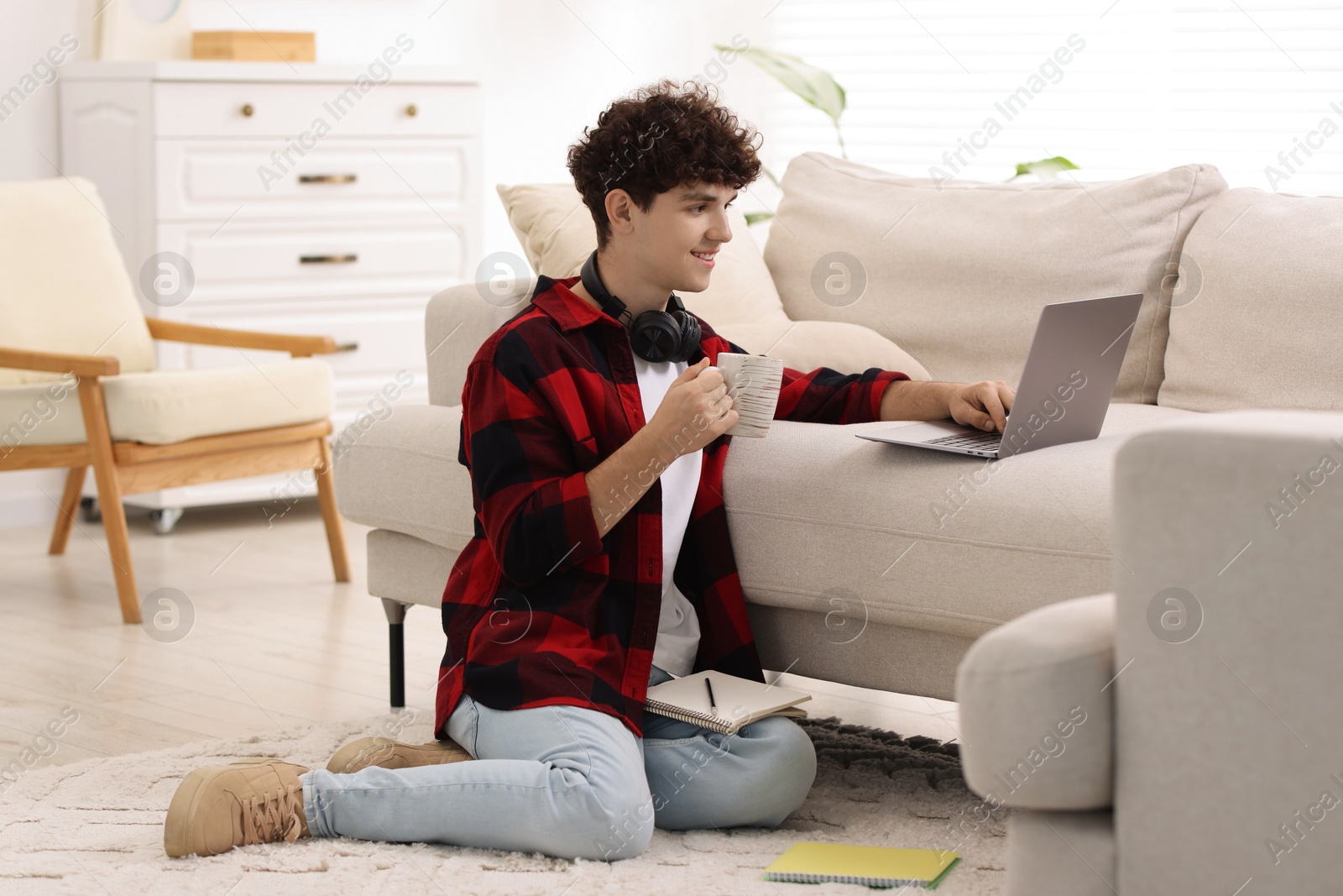 Photo of Teenager with cup of drink working on laptop at home. Remote job