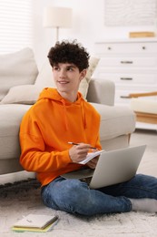 Photo of Teenager taking notes while working with laptop at home. Remote job