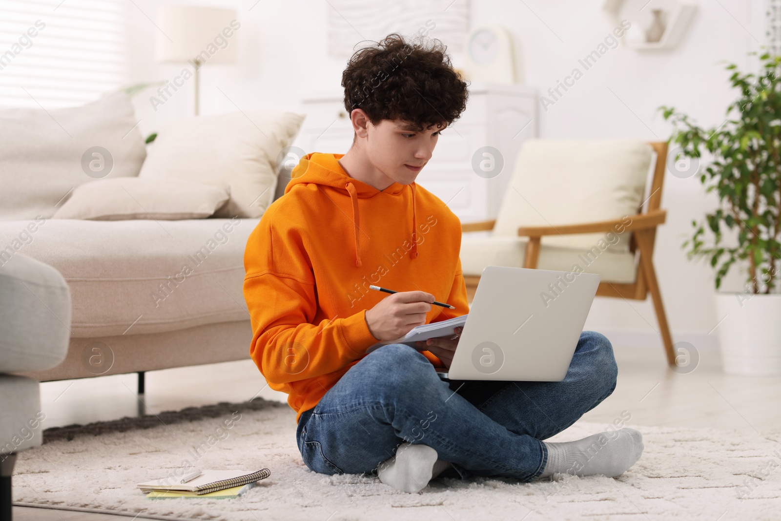 Photo of Teenager taking notes while working with laptop at home. Remote job