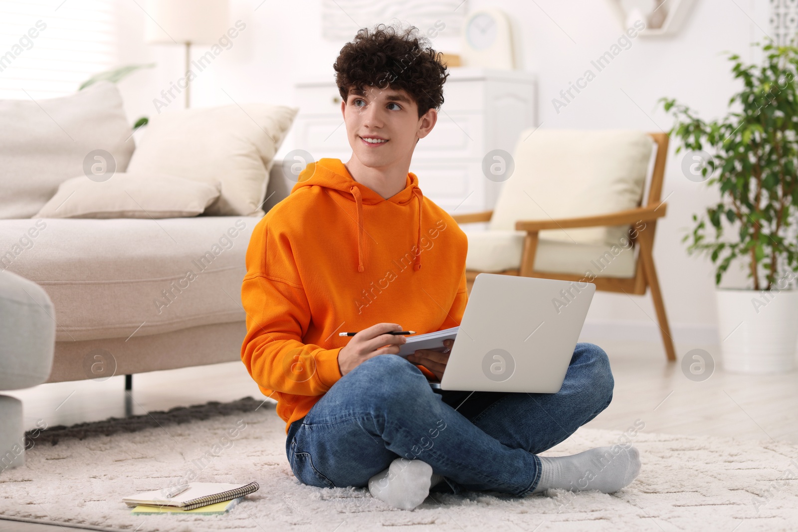 Photo of Teenager taking notes while working with laptop at home. Remote job