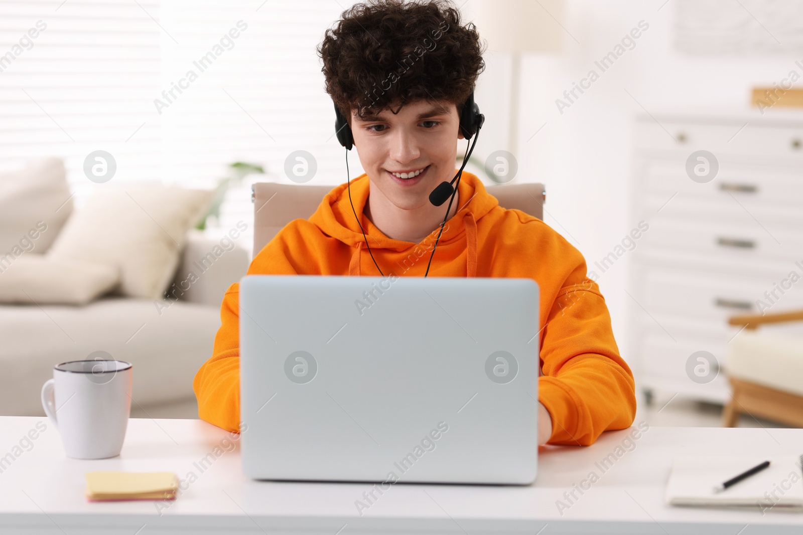 Photo of Teenager in headset working with laptop at home. Remote job