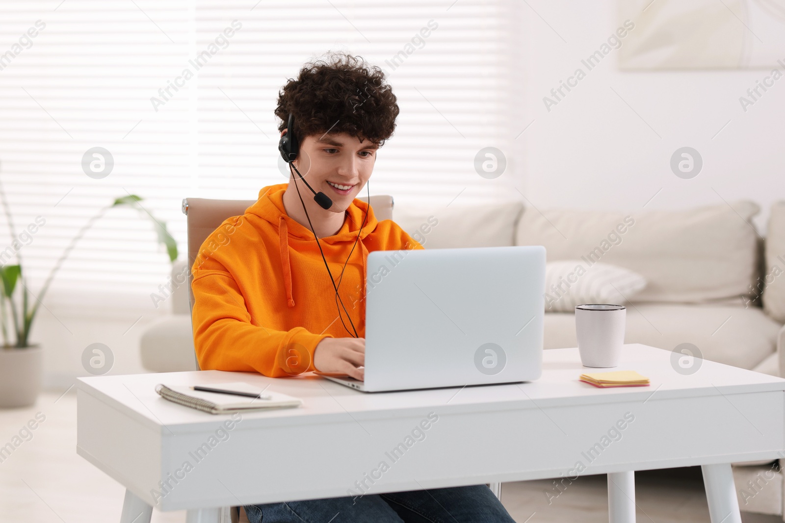 Photo of Teenager in headset working with laptop at home. Remote job