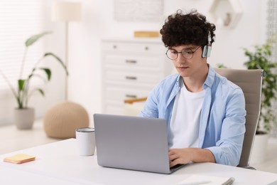 Photo of Teenager in headphones working with laptop at home. Remote job