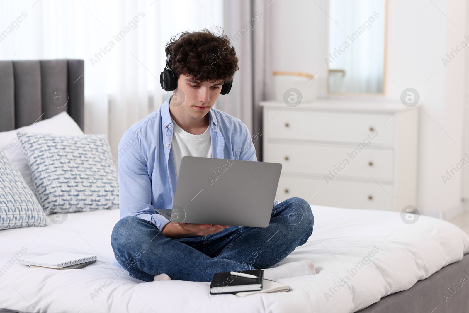 Photo of Teenager in headphones working with laptop on bed at home. Remote job