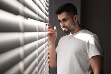 Photo of Man near window blinds at home, space for text