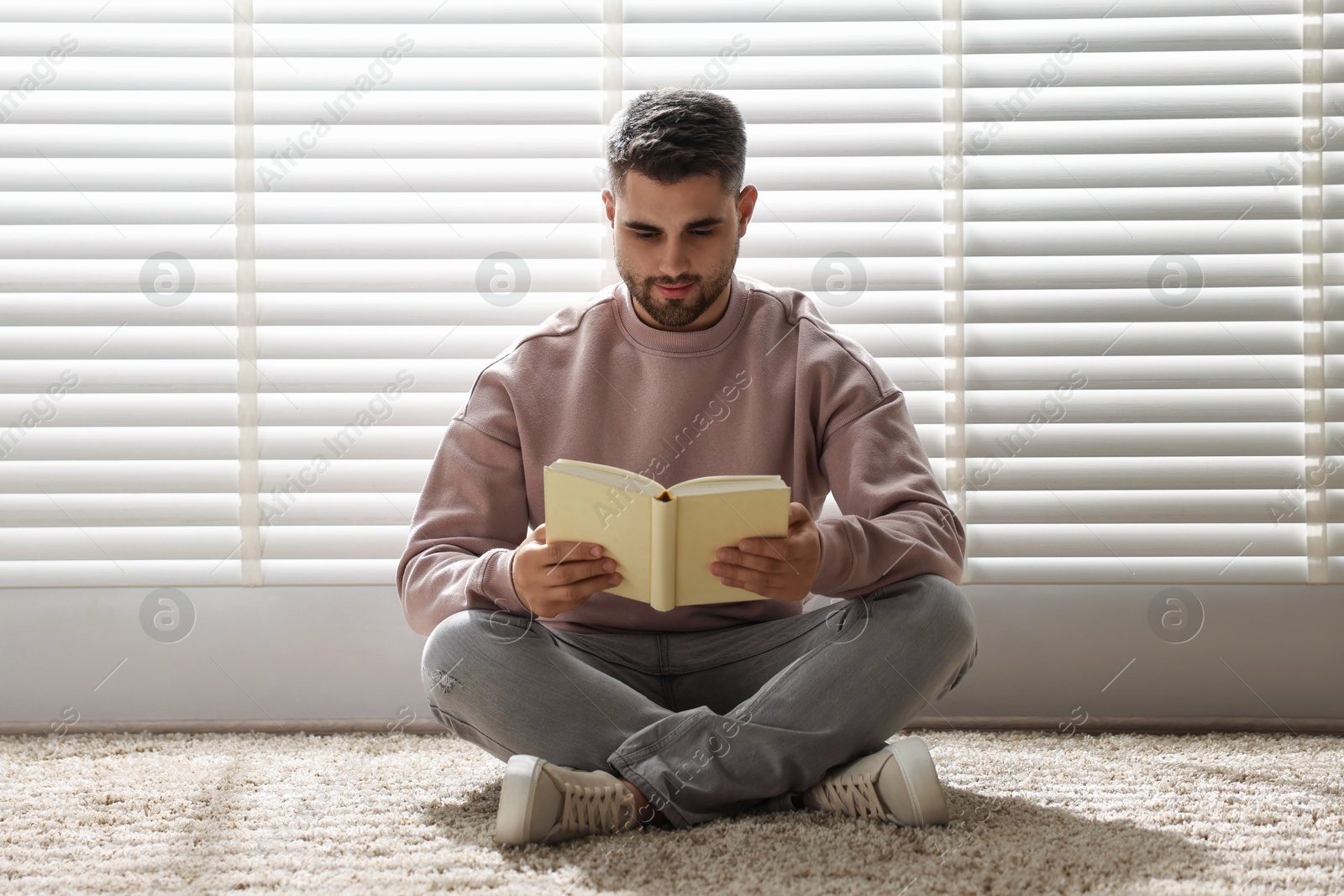 Photo of Man reading book near window blinds at home