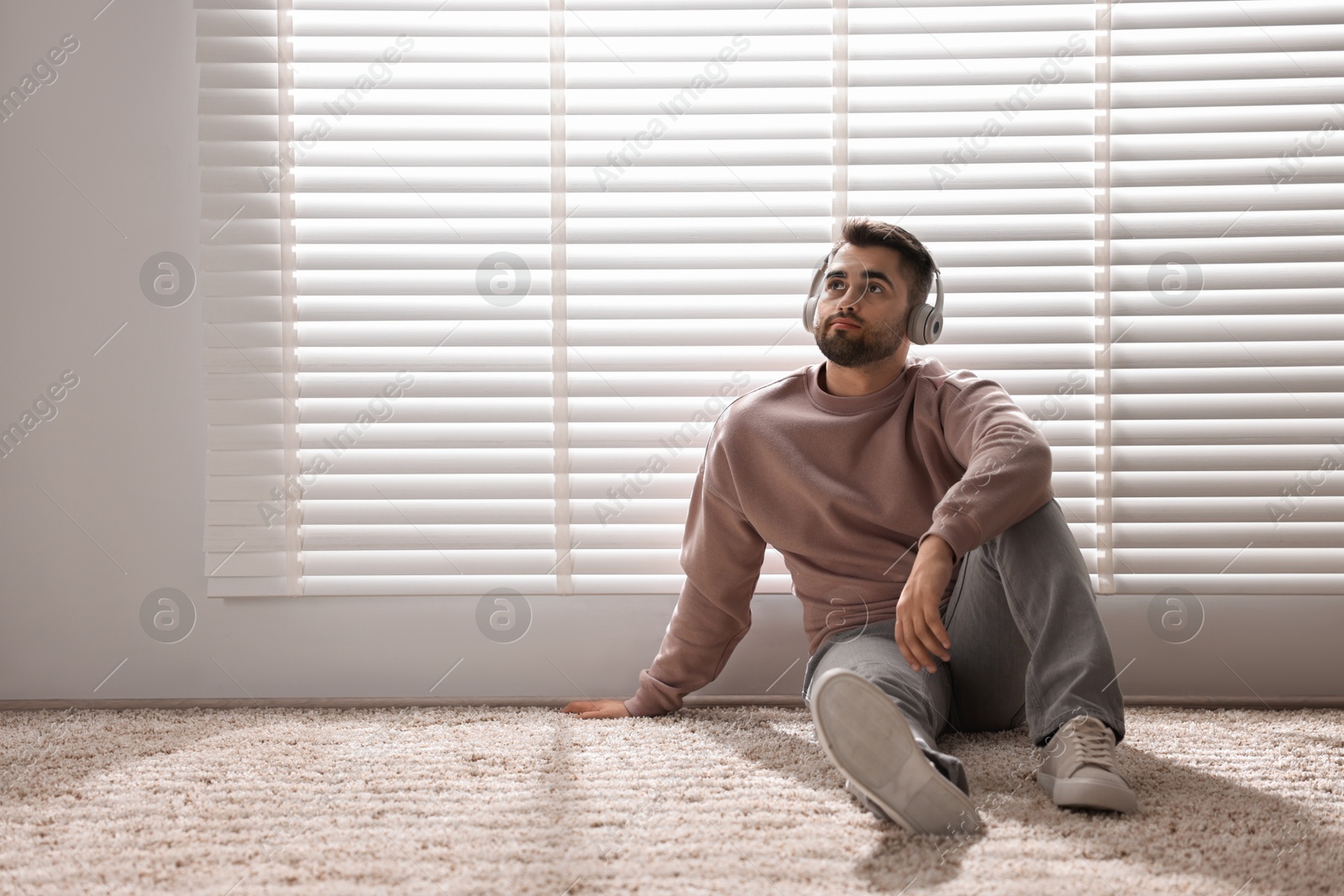 Photo of Man with headphones listening to music near window blinds at home, space for text