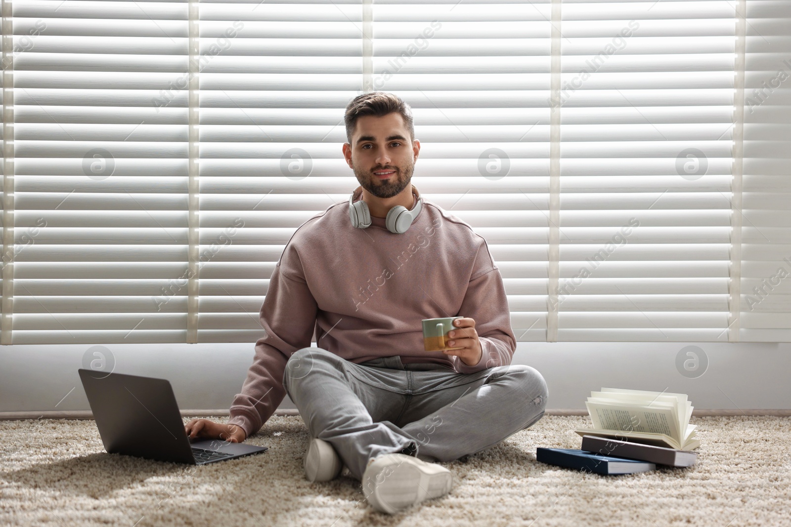 Photo of Man with laptop and books sitting near window blinds at home