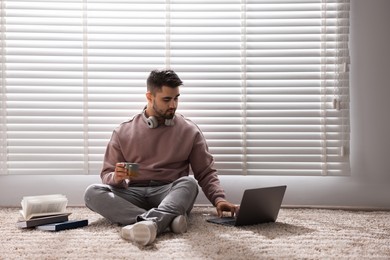 Photo of Man with laptop and books sitting near window blinds at home