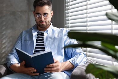 Photo of Man reading book near window blinds indoors