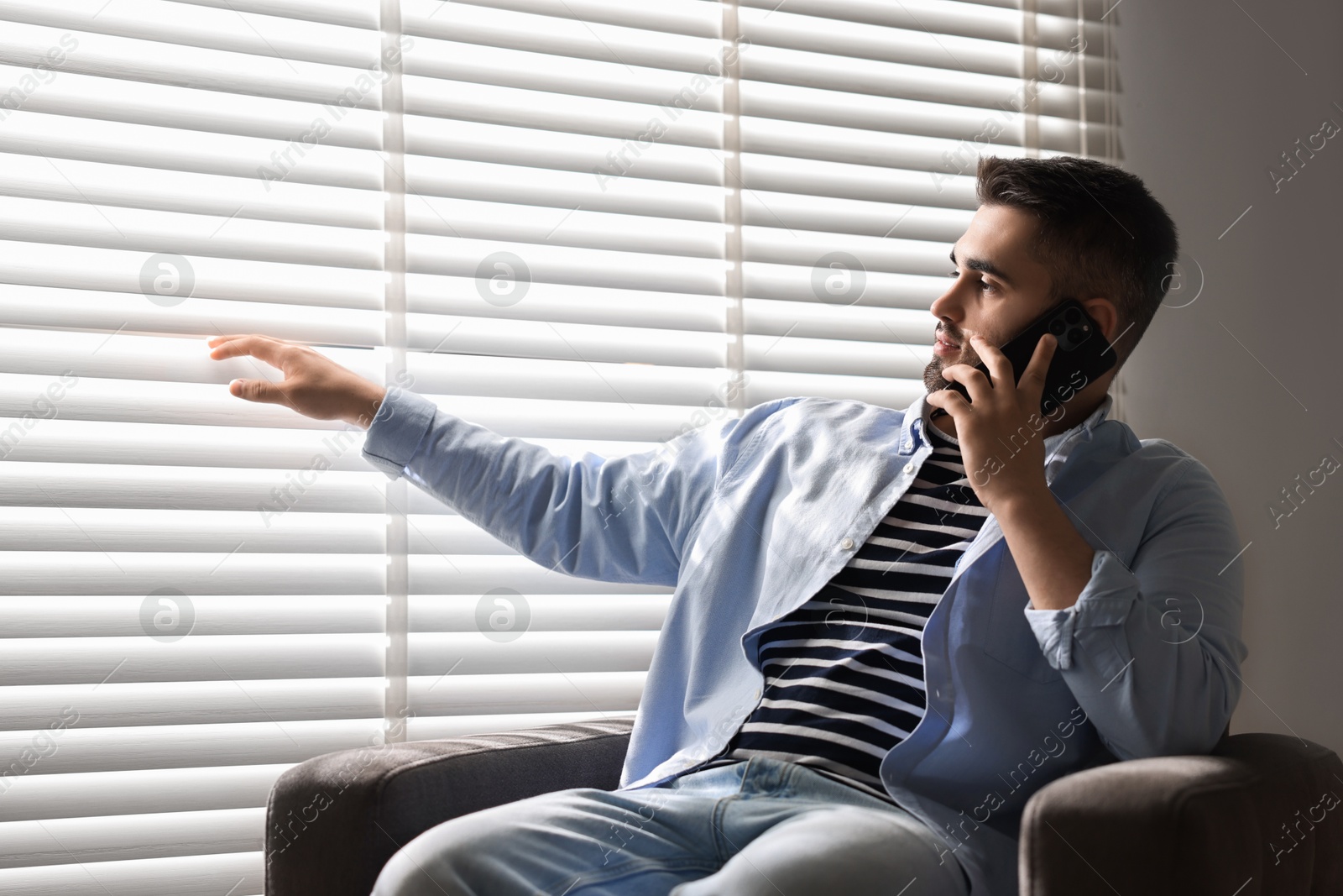 Photo of Man talking on phone near window blinds at home