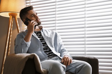Photo of Man talking on phone near window blinds at home