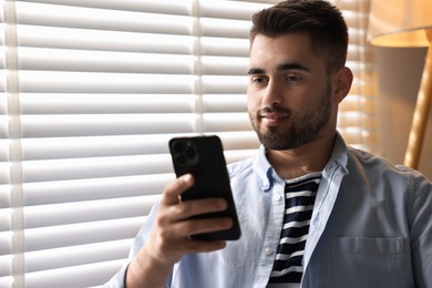 Photo of Man using smartphone near window blinds at home