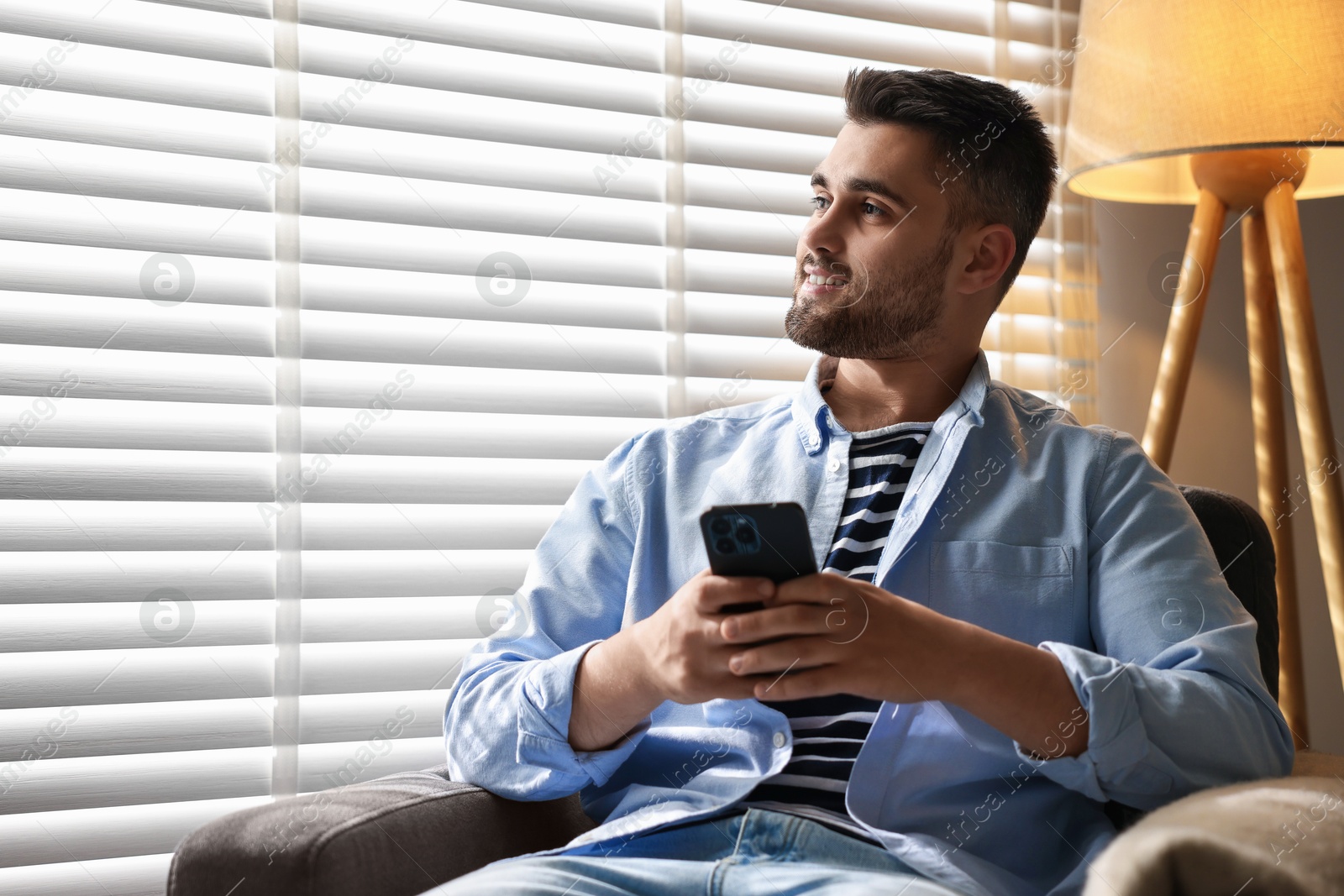 Photo of Man using smartphone near window blinds at home