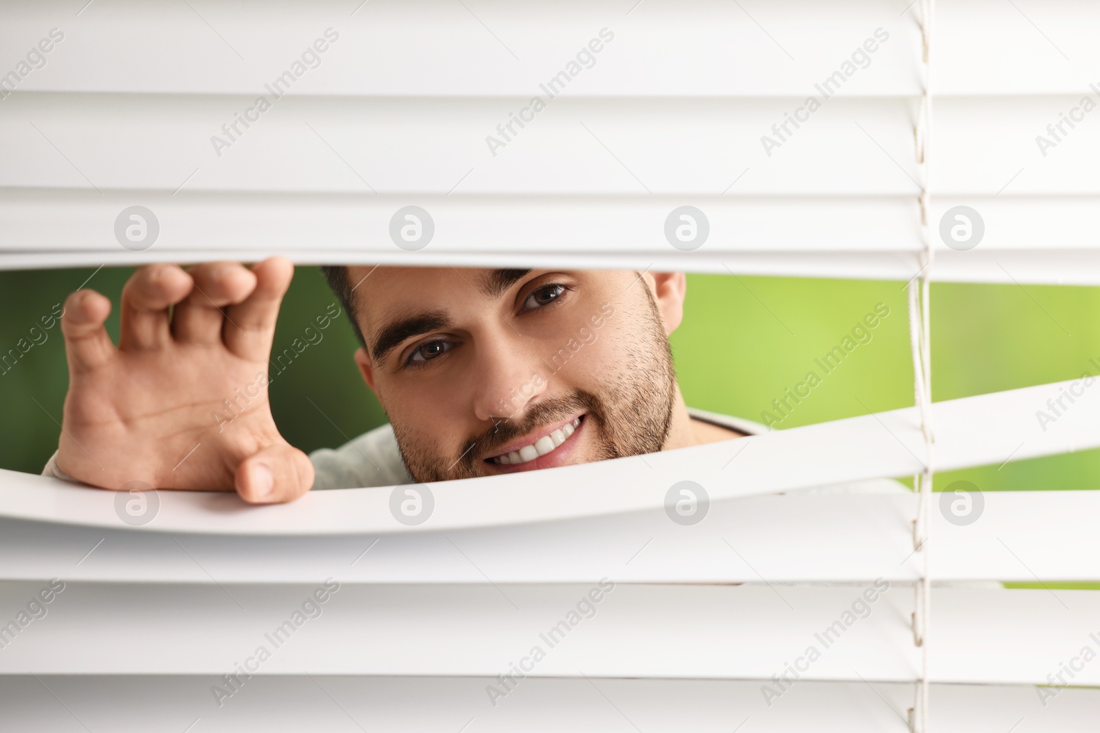 Photo of Young man looking through window blinds on blurred background