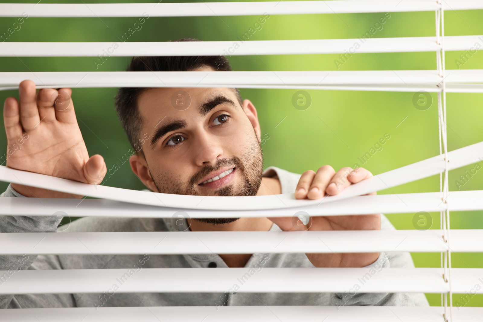 Photo of Young man looking through window blinds on blurred background