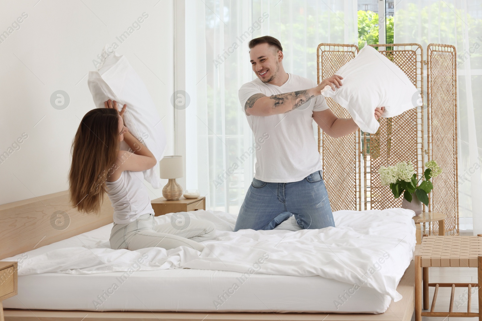 Photo of Happy couple having pillow fight on bed at home