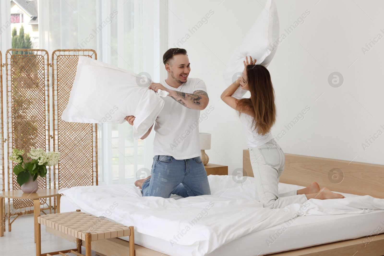 Photo of Happy couple having pillow fight on bed at home