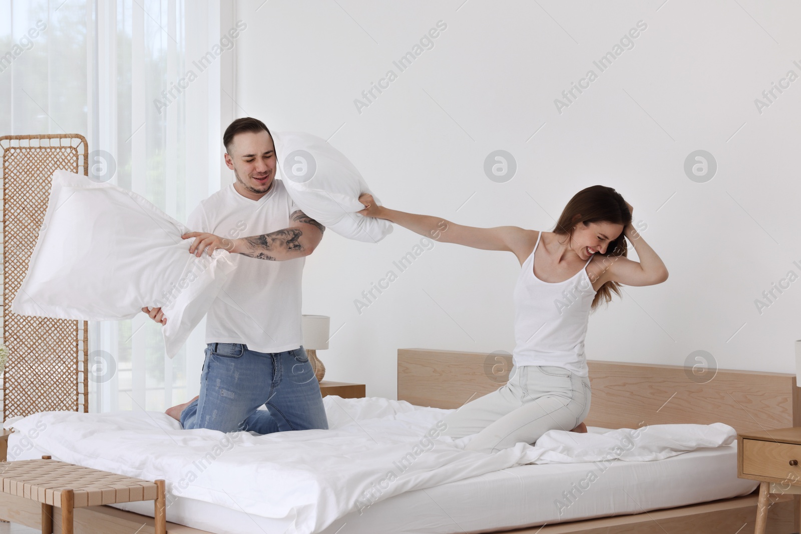 Photo of Happy couple having pillow fight on bed at home