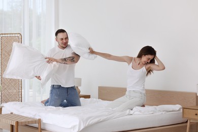 Photo of Happy couple having pillow fight on bed at home