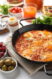 Photo of Tasty shakshouka in frying pan and other meals served for breakfast on white table, closeup