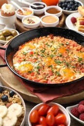 Tasty shakshouka in frying pan and other meals served for breakfast on wooden table