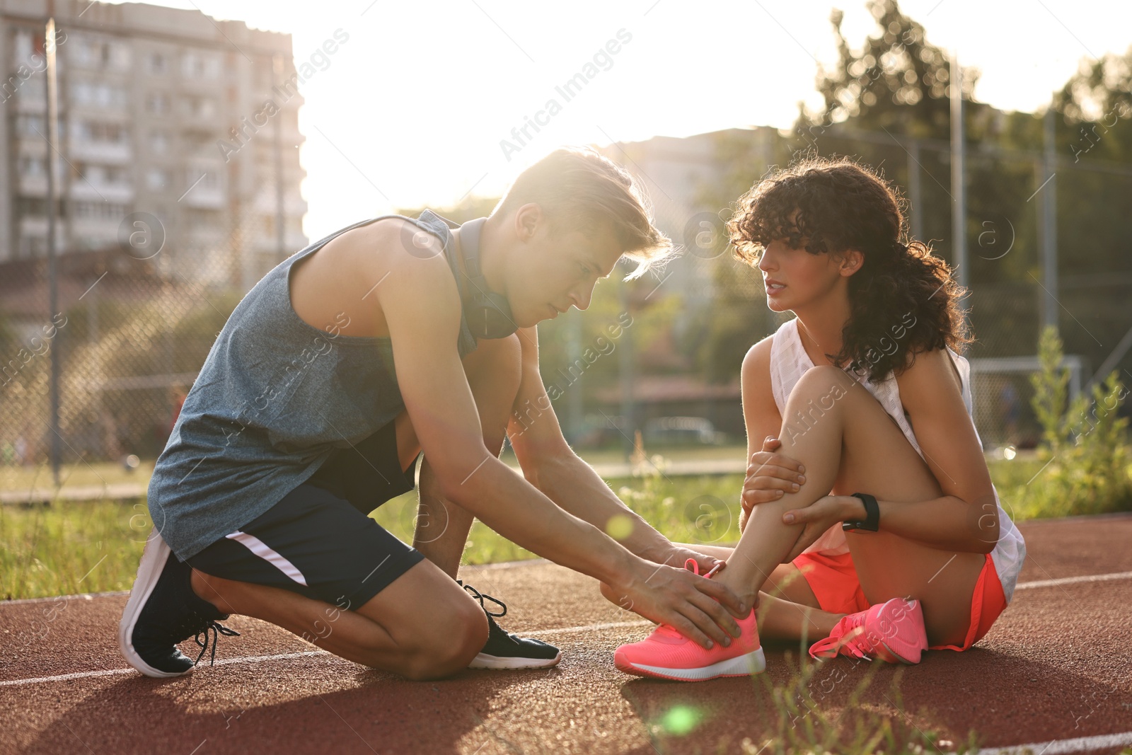 Photo of Sports injury. Man helping woman with leg pain at stadium